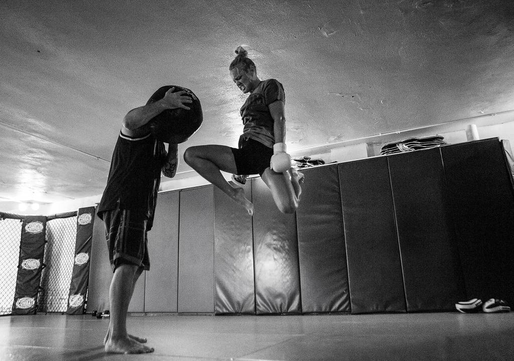 Miranda Granger jumps in the air to knee a medicine ball, held by trainer and gym owner Charlie Pearson, during her training session at Charlies Combat Club on July 26 in Everett. (Olivia Vanni / The Herald)