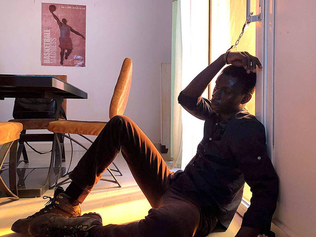 A young detective played by Amadou Mbow in Atlantics finds himself cuffed to a sliding glass door while investigating strange events in Dakar. (Frakas Productions)