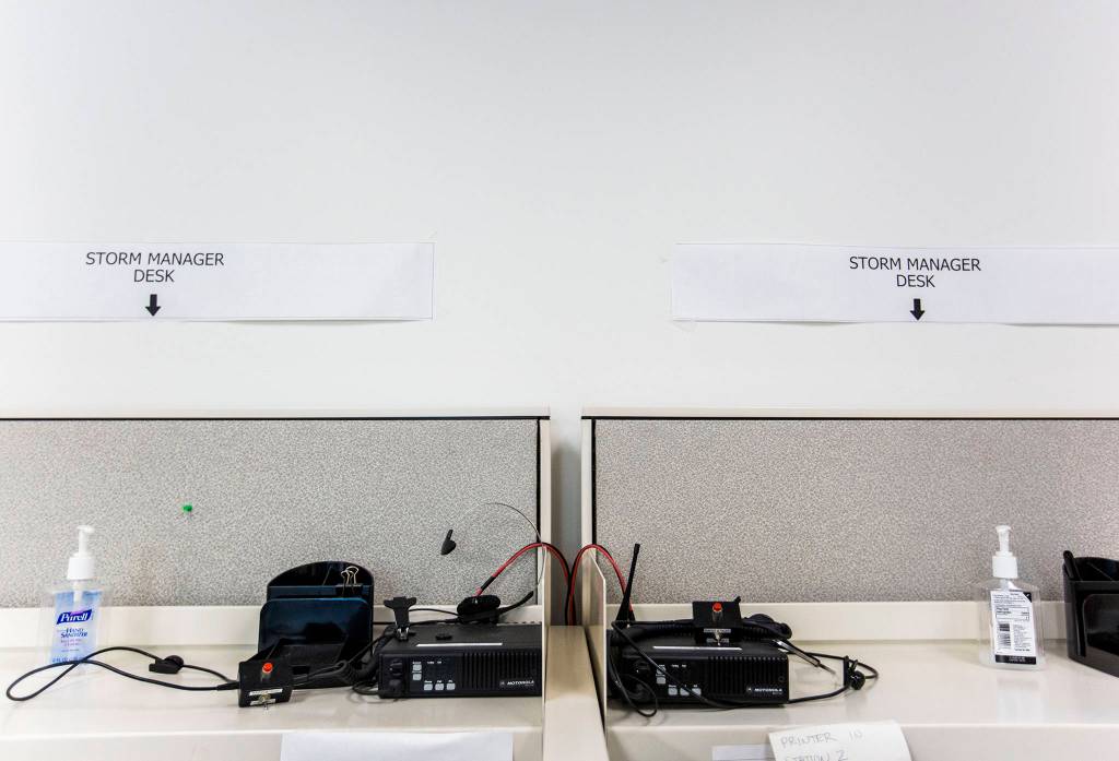 Storm Manager labels sit above radios and hand sanitizer on desks in the nerve room at the Snohomish County PUD Operations Center in Everett. (Olivia Vanni / The Herald)