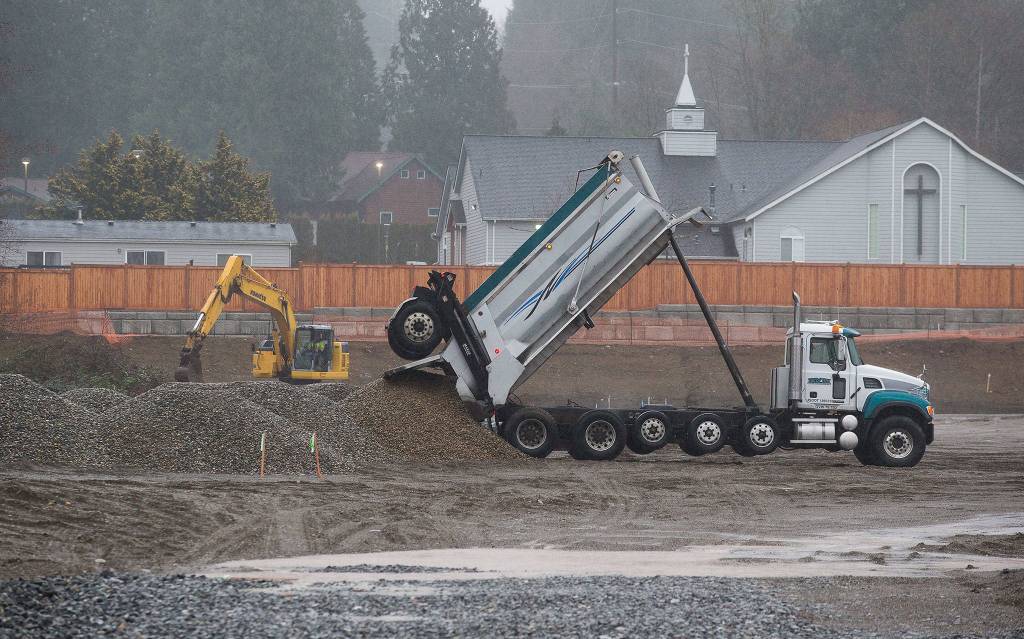 A dump trunk drops off a load of gravel as an excavator moves dirt on Monday, preparing land for new apartments at 67th Ave. NE. (Andy Bronson / The Herald)