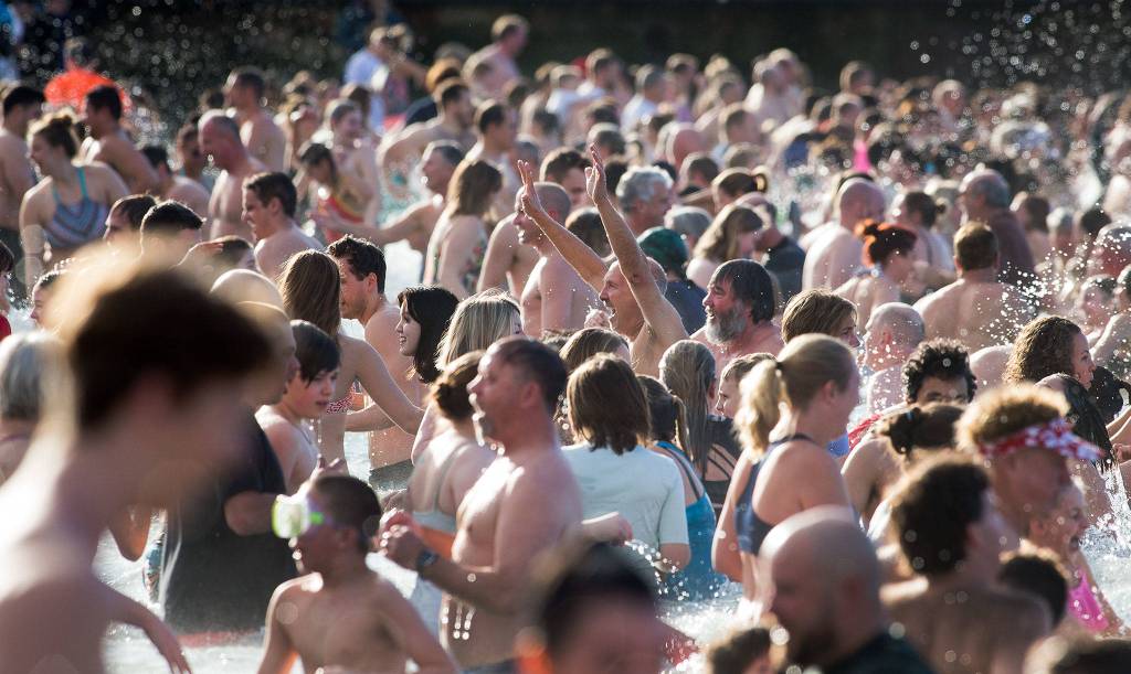 As others head in, a man raises his arms in celebration as he exits Puget Sound at the annual Polar Bear Plunge at Bracketts Landing on Wednesday in Edmonds. (Andy Bronson / The Herald)
