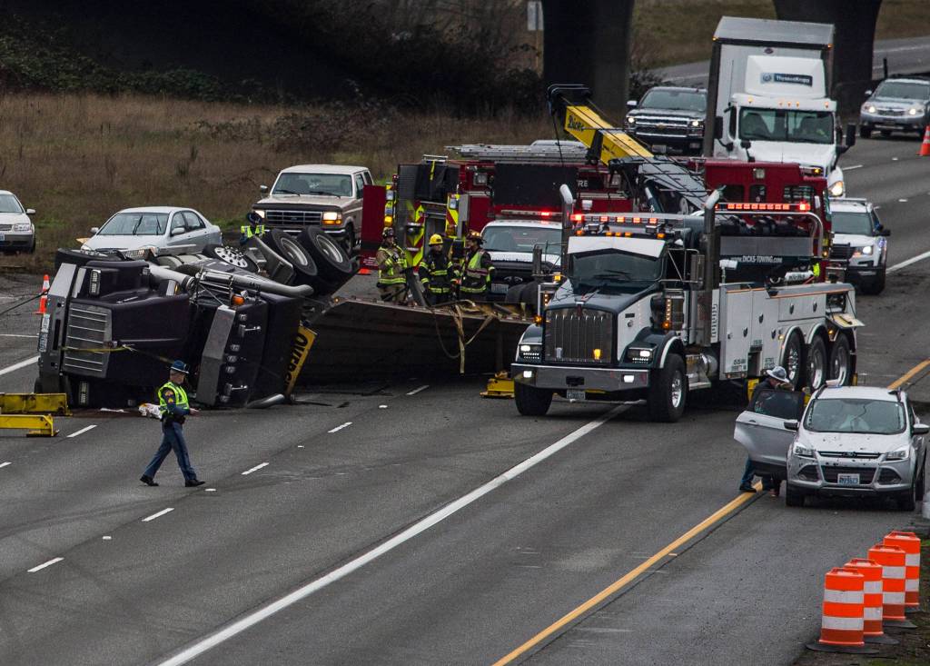 A Washington State Patrol officer walks past a flipped semi as people work to clear the flipped vehicle on northbound I-5 on Thursday in Lynnwood. (Olivia Vanni / The Herald).
