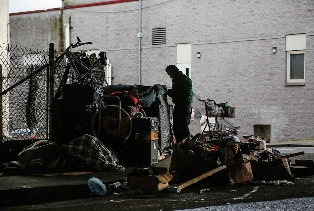 A man secures tarps over personal belongings beneath Interstate 5 overpass next to the Everett Gospel Mission, Tuesday. (Dan Bates / The Herald)