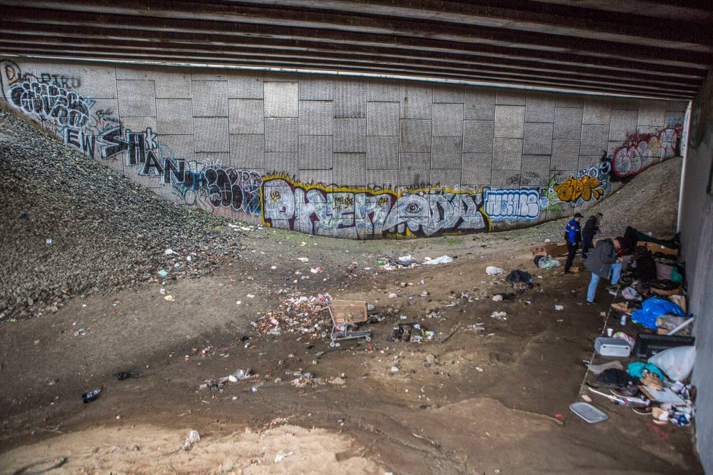 Everett police officers and social workers talk with people experiencing homelessness in the area known as The Pit on Thursday. (Olivia Vanni / The Herald)