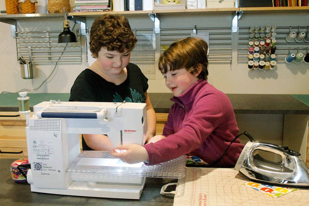 Bella Bond (left), 10, and Arya Bochantin,7, work on the sewing machine together.(Kira Erickson / Whidbey News-Times)