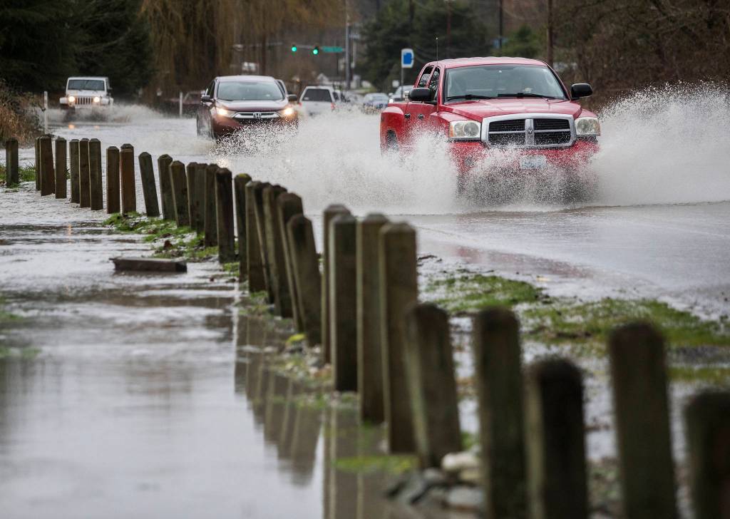 A truck drives through water running over State Route 530 next to Twin Rivers County Park on Saturday in Arlington. (Olivia Vanni / The Herald)