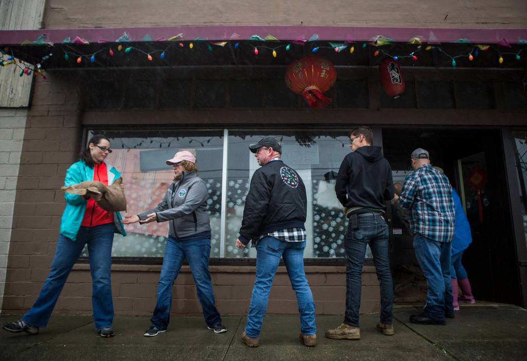 Local resident volunteers sandbag the entrance to a restaurant as water begins to make its way up Main Street on Saturday in Sultan. (Olivia Vanni / The Herald)