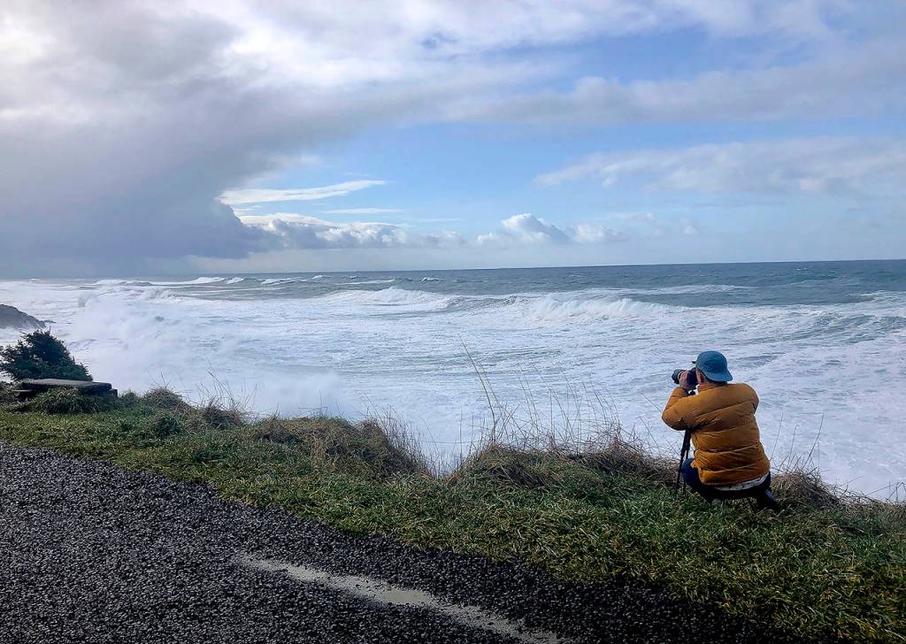 In this Jan. 11 photo, a man photographs waves crashing onto the cliffs at Rodea Point in Lincoln County, Oregon. during an extreme high tide that coincided with a big winter storm. (AP Photo/Gillian Flaccus)