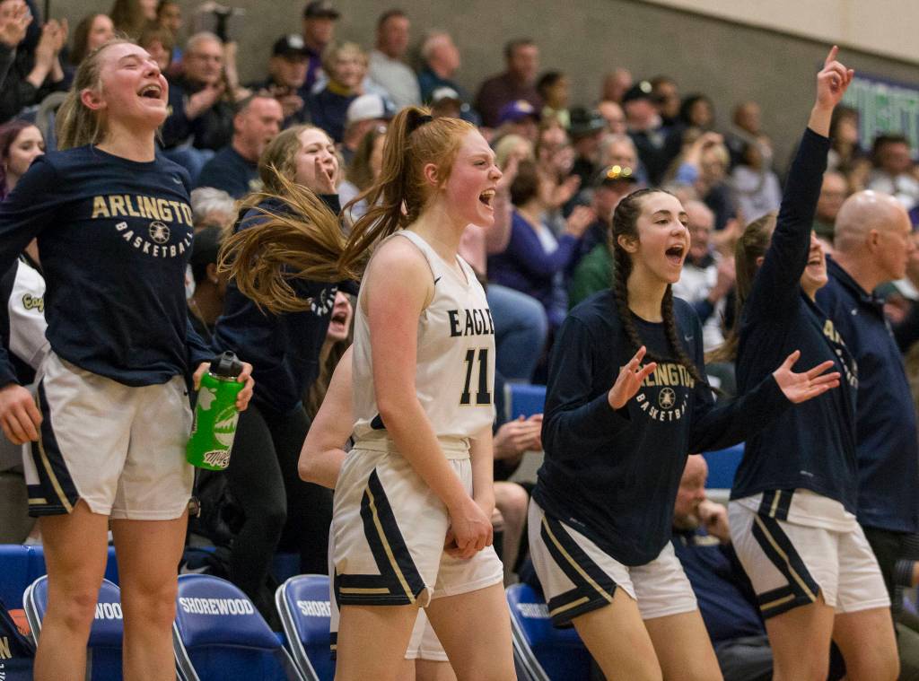 The Arlington bench reacts to a teammate making a 3-point shot during a 3A state regional game against Lake Washington on Saturday in Shoreline. (Olivia Vanni / The Herald)