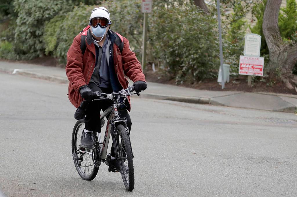 Ted S. Warren / Associated Press                                A man wearing a mask and goggles rides his bike out of the parking lot at the Life Care Center in Kirkland on Tuesday. The facility has been tied to several confirmed cases of the COVID-19 coronavirus.