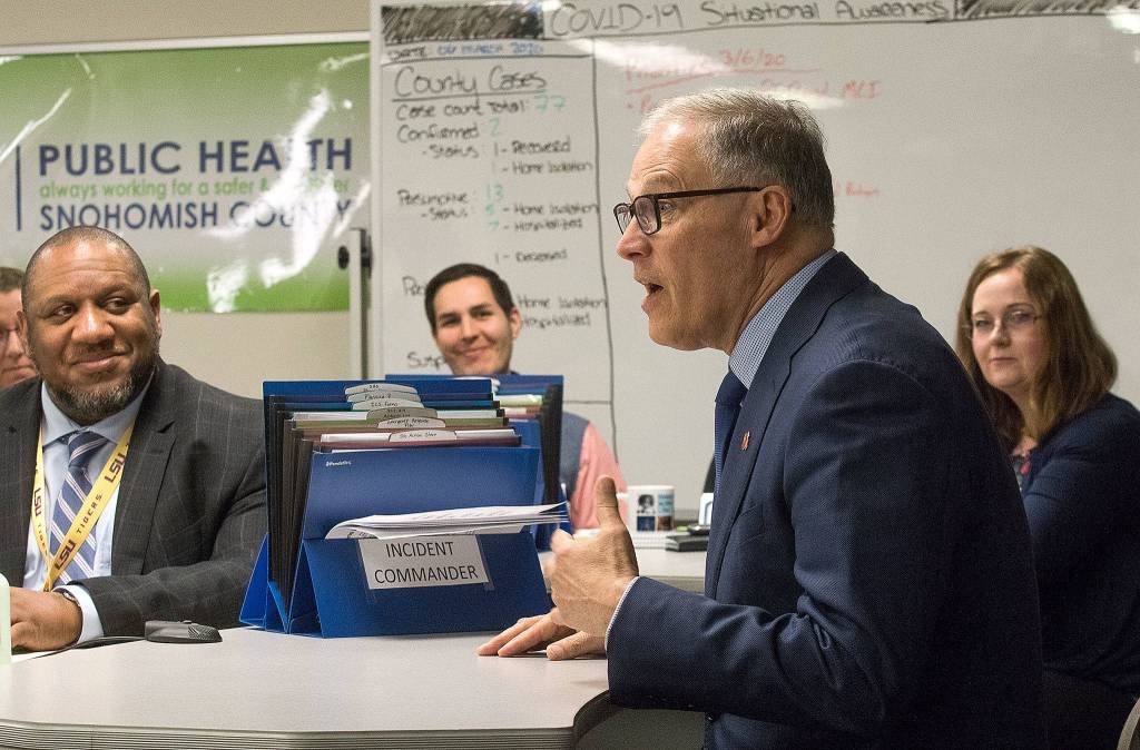 Daily statistics on a board list county cases of the coronavirus as Governor Jay Inslee talks with staff at the Snohomish Health Districts Incident Command Center on Friday in Everett. (Andy Bronson / The Herald)