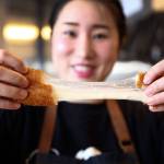 Aram Han demonstrates the stringy properties of the cheese inside a mozza hot dog at Seoul Hotdog. (Kevin Clark / The Herald)
