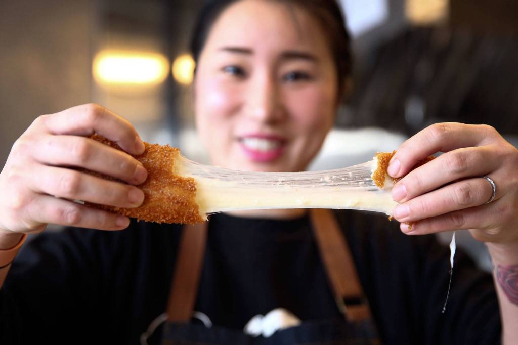 Aram Han demonstrates the stringy properties of the cheese inside a mozza hot dog at Seoul Hotdog. (Kevin Clark / The Herald)