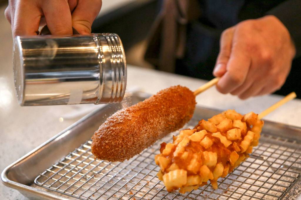 Co-owner Sean Lee sprinkles sugar on corn dogs at Seoul Hotdog in Lynnwood. (Kevin Clark / The Herald)