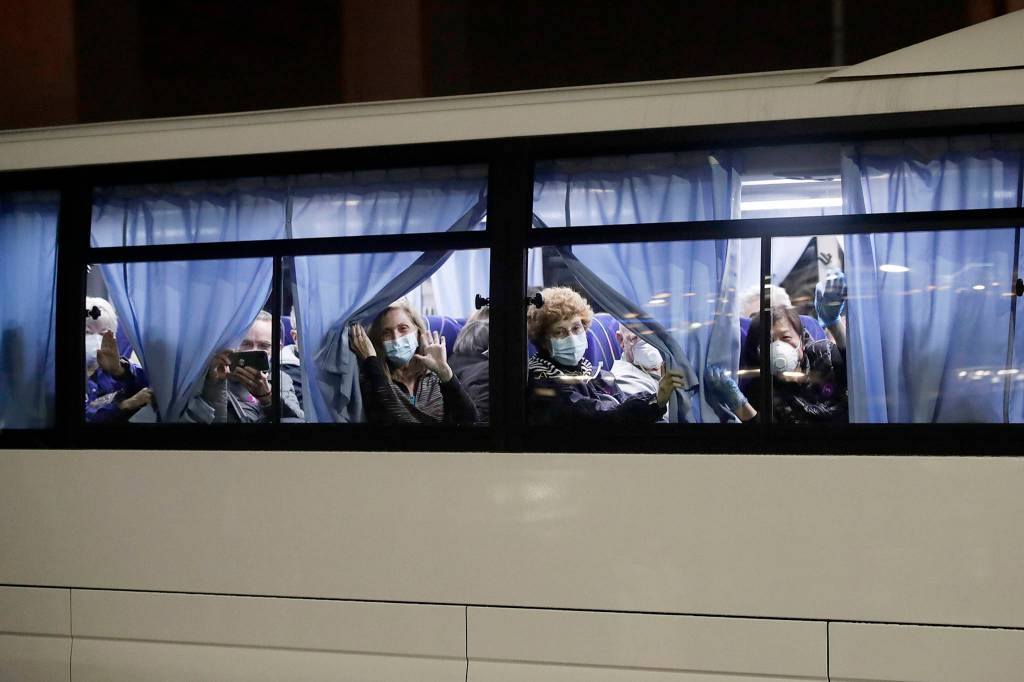 Susan Anabel (center) waves at the media as buses carry her and other passengers from the quarantined Diamond Princess cruise ship at a port in Yokohama, near Tokyo, on Feb. 17. (AP Photo/Jae C. Hong)