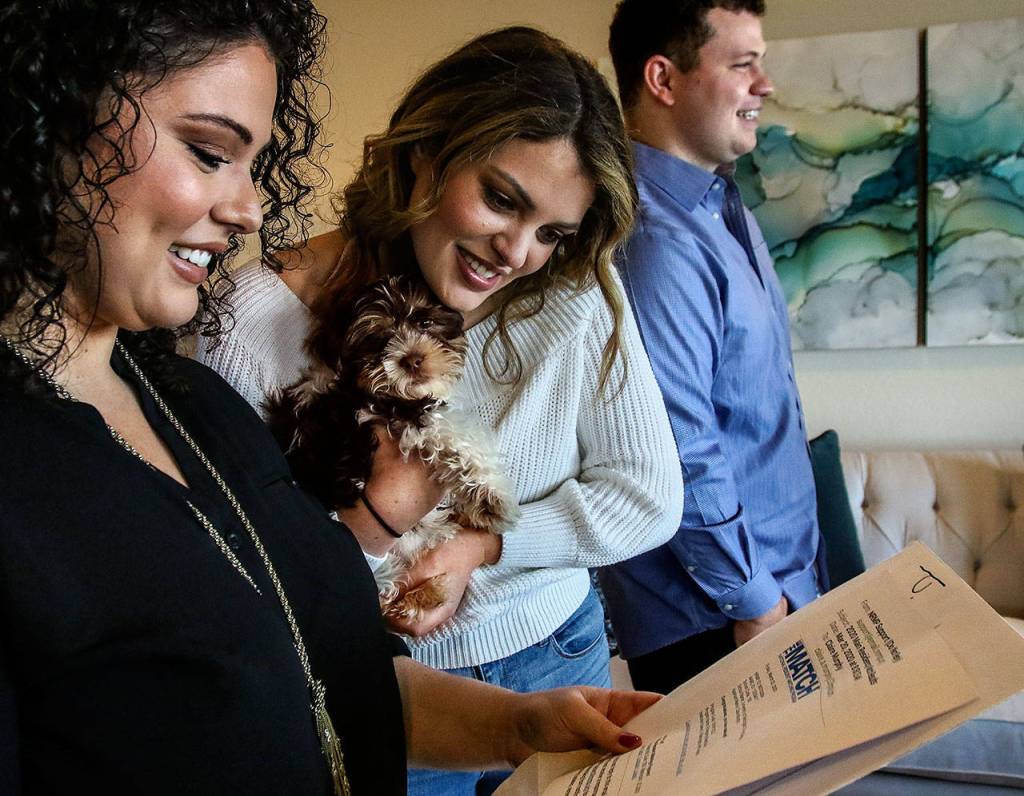 Sisters Claire and Olivia Murphy read the official Match email announcing Claires selection by the University of Washington for her medical residency. Olivia holds their dog, Teddy, while their brother Kevin joins in the celebration Friday at the familys Everett home. (Dan Bates / The Herald)