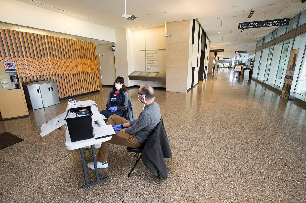 In a normally bustling hospital lobby, Amanda Ray and Deniz Campbell man a security screening desk at Providence Regional Medical Center on Friday, March 20, 2020 in Everett, Wa.(Andy Bronson / The Herald)
