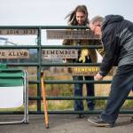 Jennifer Thompson, left, and her father Ron Thompson secure a new remembrance plaque to the Oso slide site gate on Sunday, near Oso. Ron Thompson handcrafts a new plaque for the gate every year. (Olivia Vanni / The Herald)
