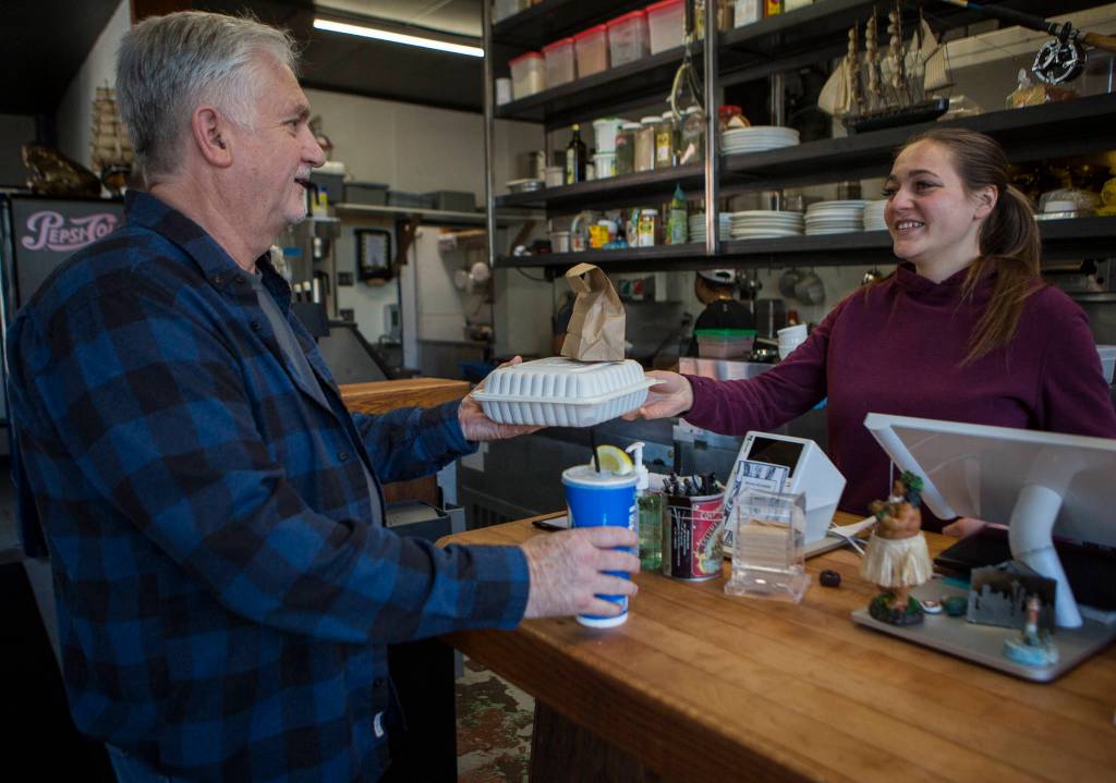 Andys Fish House employee Kate Gordon hands customer Andy Coleman his to-go order on March 19 in Snohomish. (Olivia Vanni / The Herald)