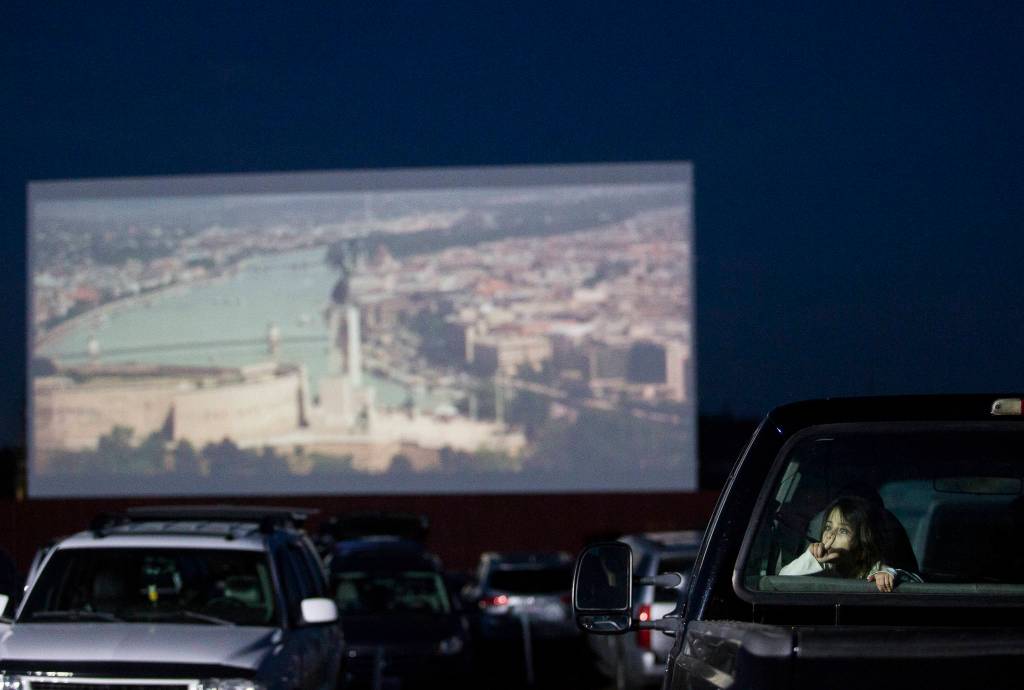 A young girl plays in in the back seat of a pick-up truck as movie previews play on the drive-in screen on Thursday. (Olivia Vanni / The Herald)