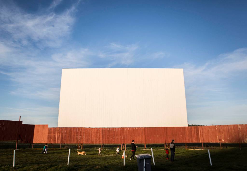 Children run around at the base of the Blue Fox Drive-In screen as the sun begins to set on Thursday in Oak Harbor. (Olivia Vanni / The Herald)