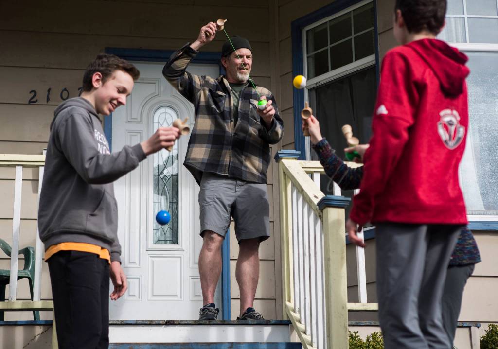 Zach Leader, center, learns how to use a kendama with his kids Saturday as they enjoy the sunshine outside of their home in Everett. (Olivia Vanni / The Herald)