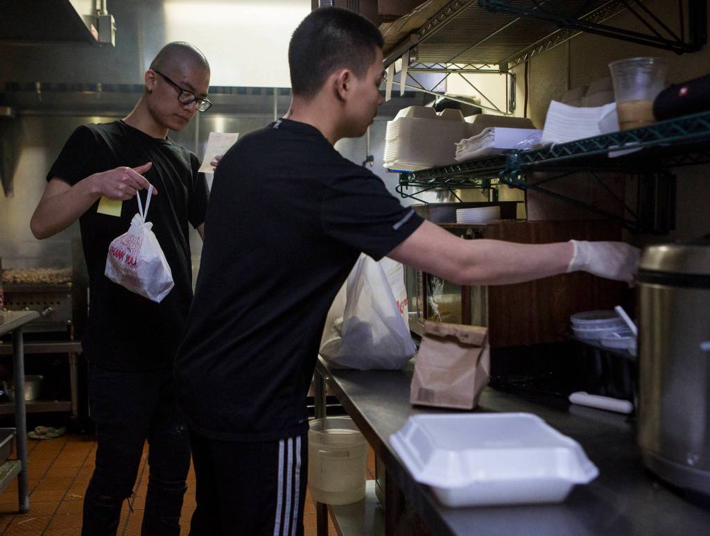 Anthony Luong (left) checks an order ticket while Brian Le works on packaging up food at Basil Authentic Vietnamese Cuisine on April 5 in Everett. (Olivia Vanni / The Herald)
