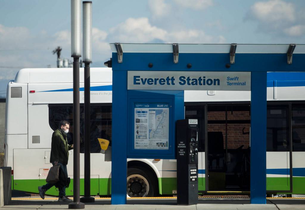 A man wearing a face mask walks toward the rear door of a Community Transit bus at the Everett Station on March 20 in Everett. (Olivia Vanni / The Herald)