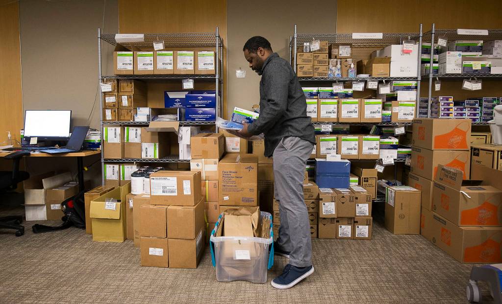 In a board room turned into a logistics center, Ian Smith organizes protective gear and gets it ready for distributing to various medical personnel at Providence Regional Medical Center on March 20 in Everett. (Andy Bronson / The Herald)