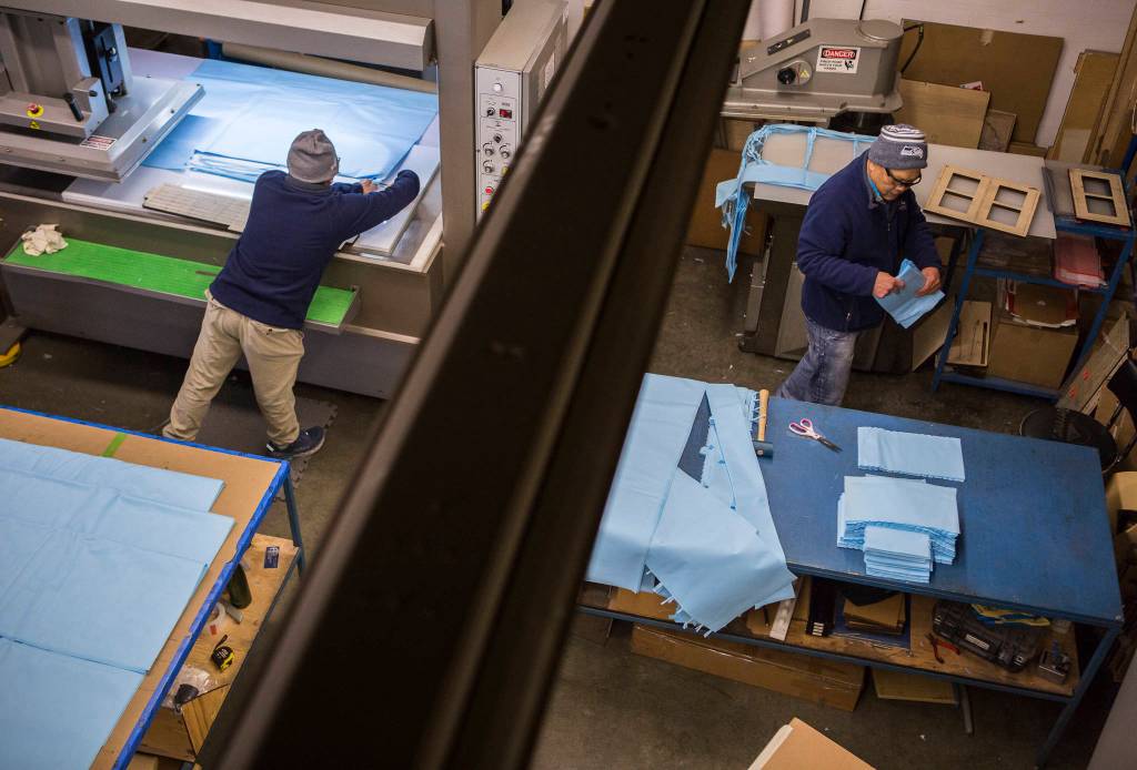 The Nguyen (left) and Theo Nguyen (right) cut out face mask parts from surgical wrap at Terrene, Inc. on March 27 in Mukilteo. (Olivia Vanni / The Herald)