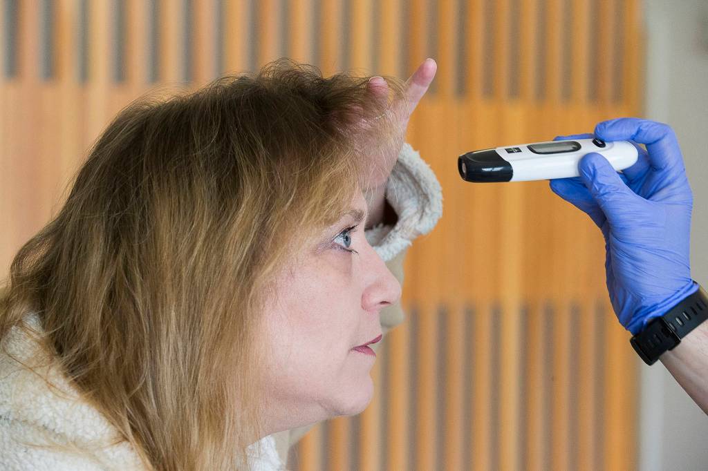 Susan Kaylor pulls her hair back to have her forehead temperature taken at Providence Regional Medical Center on March 20 in Everett. (Andy Bronson / The Herald)