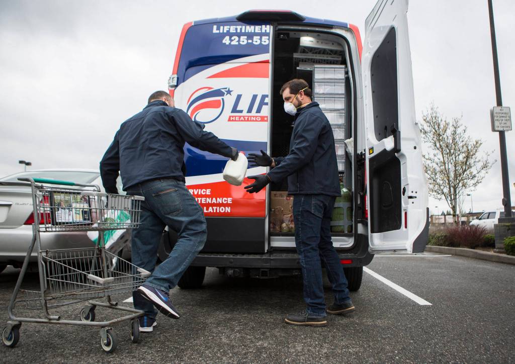 Dwight Miller (left) and Darrick Philp (right) load groceries into their Lifetime Heating and Air company van for delivery on March 27 in Snohomish. (Olivia Vanni / The Herald)