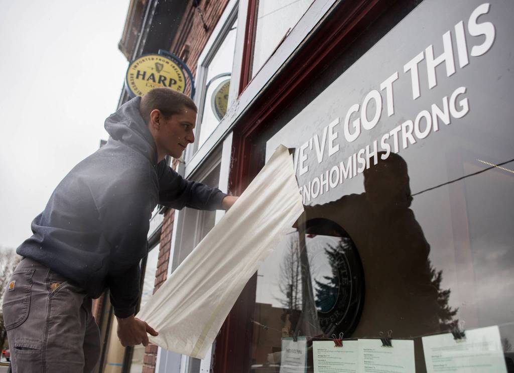 Ethan Spain finishes putting a temporary vinyl on Freds Rivertown Ale House window with the phrase, weve got this #snohomishstrong on Friday in Snohomish. (Olivia Vanni / The Herald)
