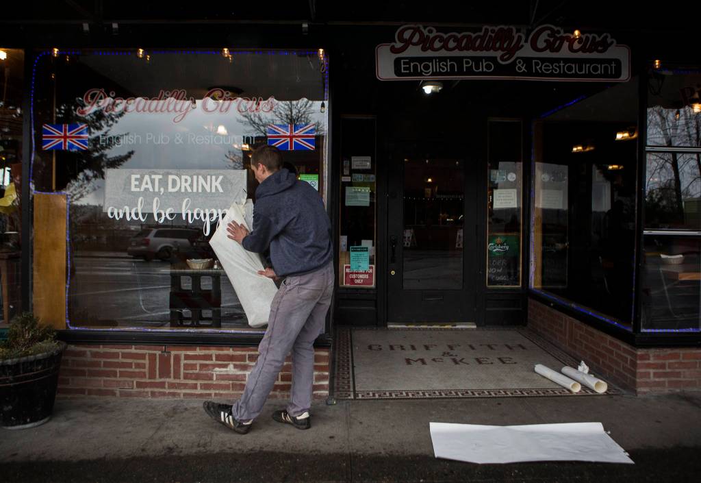 Ethan Spain puts a temporary vinyl on the front window of Piccadilly with the phrase, eat, drink and be happy Friday in Snohomish. (Olivia Vanni / The Herald)