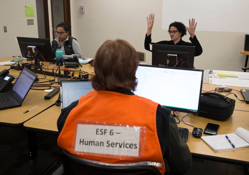 Alessandra Durham (right) talks with teammates Simone Tarver (left) and Jackie Anderson about the Isolation and Quarantine Facility while working at the Snohomish County Emergency Management Center on March 30 in Everett. (Andy Bronson / The Herald)