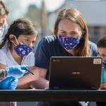 Jody Urban, left, helps Michelle Nunez setup a Chromebook at Frank Wagoner Elementary School as her daughter Lilah, left, and son Oilver watch. Students and their families picked up computers for online learning on Wednesday. (Andy Bronson / The Herald)