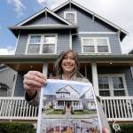 In this April 1 photo, Rebeka McBride holds a picture of her home as she poses in front of it in Monroe, Washington. She put her house on the market in early March and is in the process of closing on the sale. (AP Photo/Elaine Thompson)