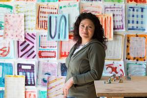 Everett artist Cat Snapp, with Covid-19 art, which she began working on before it became a pandemic, in her studio on Monday, April 13, 2020 in Everett, Wa. The wall art is mixed media on paper and the statues are abstracts made of Sculpy, a polymer clay. material. (Andy Bronson / The Herald)