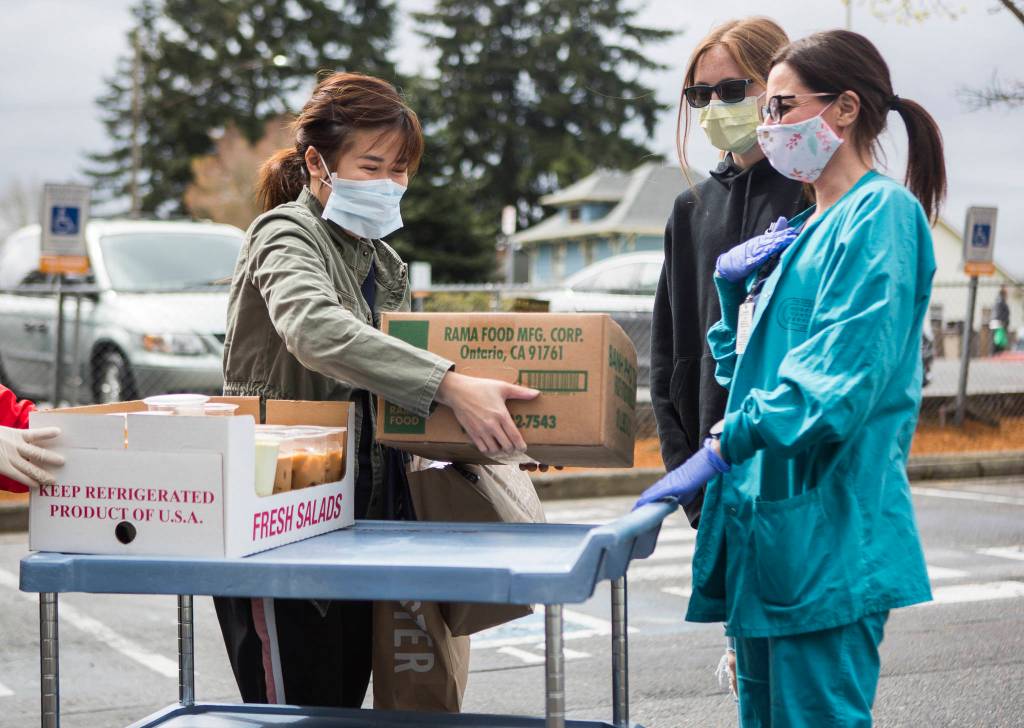 Pho Nguyen owner Cindy Nguyen (left) smiles behind her face mask as she delivers food on Saturday in Everett. (Olivia Vanni / The Herald)