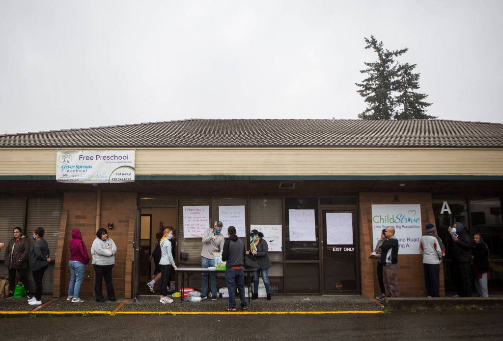 People line up and wait for their numbers to be called to pick up food April 21 outside of The Village in Everett. (Olivia Vanni / The Herald)