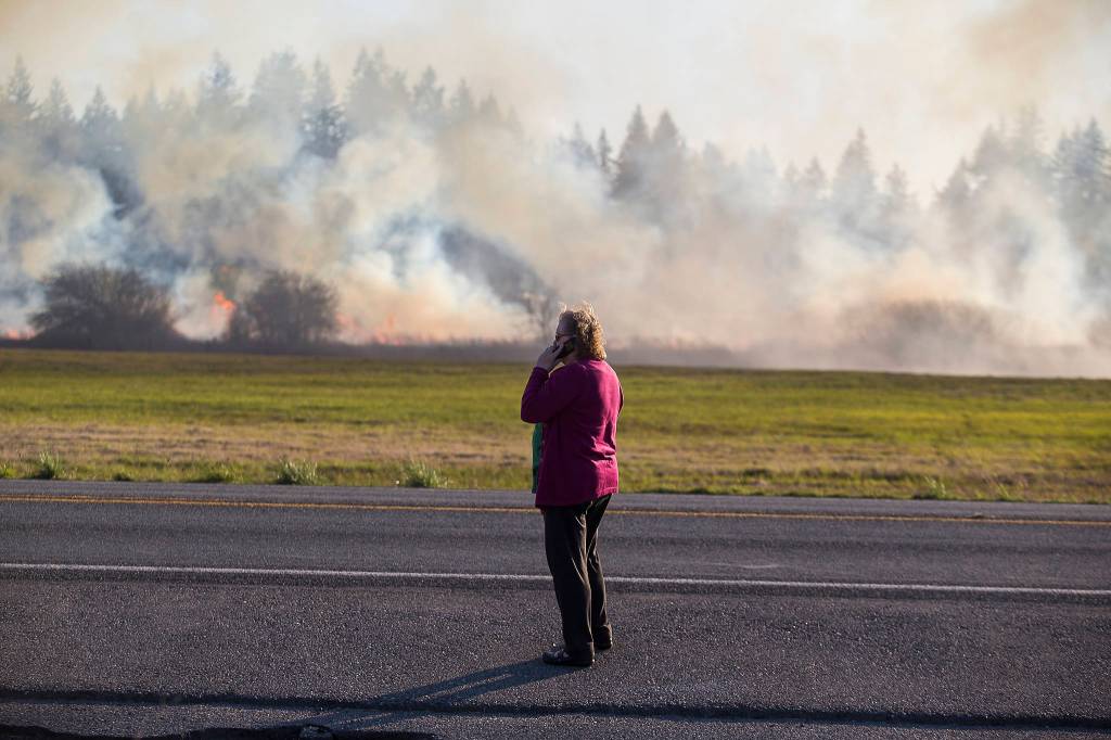 A woman watches as fire spreads across her property while multiple strike teams from Snohomish County fire departments fight a brush fire along Highway 9 on Wednesday in Bryant. (Andy Bronson / The Herald)