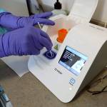 Inside in the lab at the Snohomish Health District in Lynnwood, an Abbott Rapid Test machine is used to test samples from drive-thru patients. Here, Dr. Mary Jo Kintner, a retired Edmonds family practice physician, places a swab into the machine. (Greg Gilbert / Seattle Times, pool)