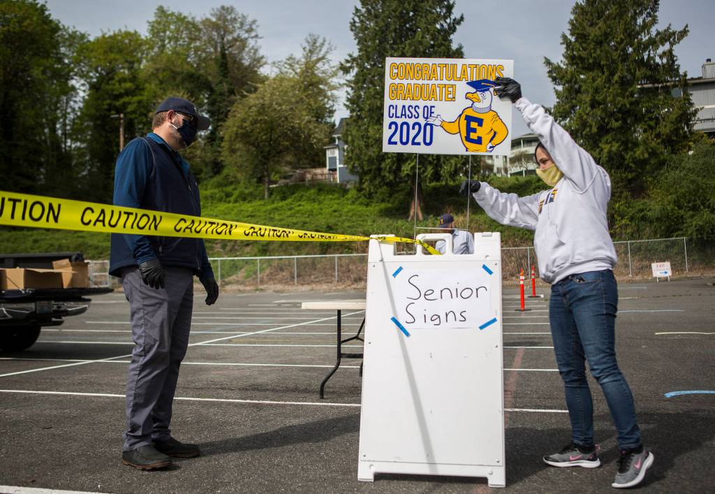 Doug Plucker (left) and Mary Ingraham (right) set up signs for seniors to pick up at the drive-thru graduation gown pickup Tuesday in Everett. (Olivia Vanni / The Herald)