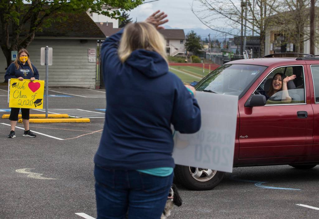 Patty Osborn (left) waves at Everett High School student Danielle Alazza while she picks up her graduation gown Tuesday in Everett. (Olivia Vanni / The Herald)