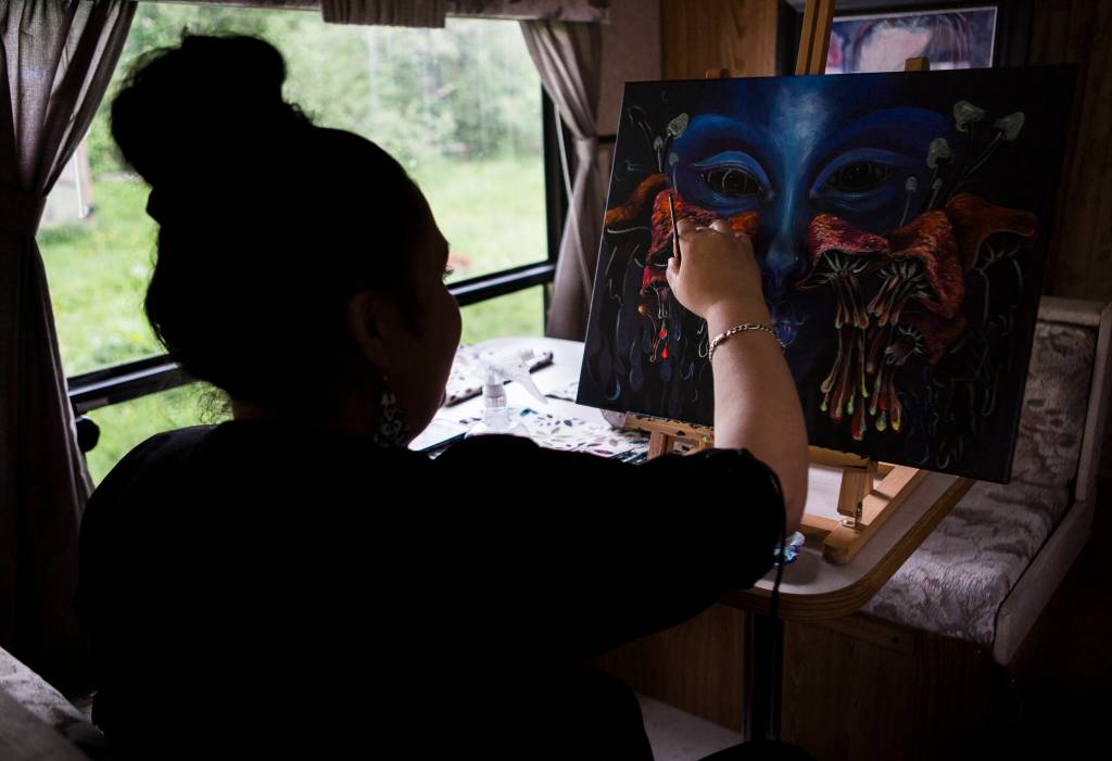 A woman works on her paintings with black light reactive acrylic paint at her home on Sunday in Everett. She is a self-taught painter who has been living and painting in Snohomish County for more than 18 years. (Olivia Vanni / The Herald)