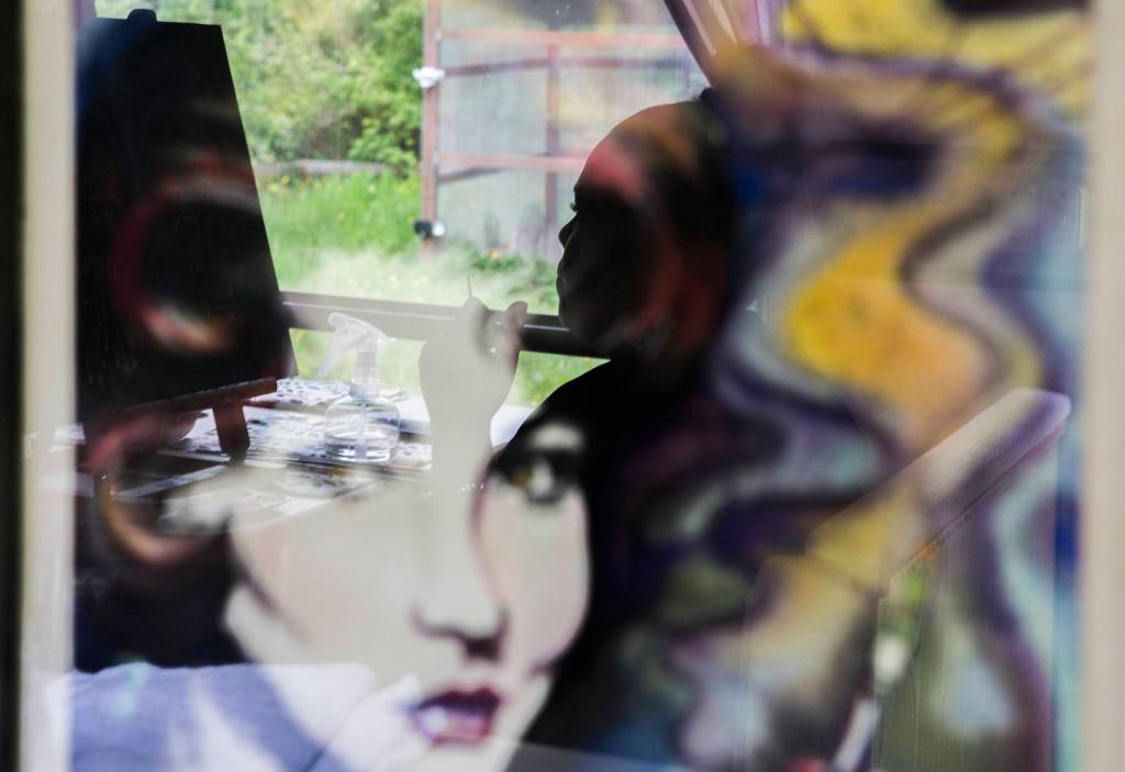 A woman is reflected in one of her older paintings as she works on a new painting at her home on Sunday in Everett. (Olivia Vanni / The Herald)