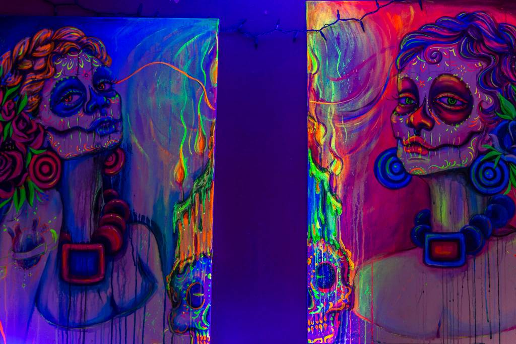 A pair of blacklight reactive acrylic paintings she recently sold hang in her studio on Sunday in Everett. Her art is her main source of income which has been hard to sell with to events being cancelled due to COVID-19. (Olivia Vanni / The Herald)