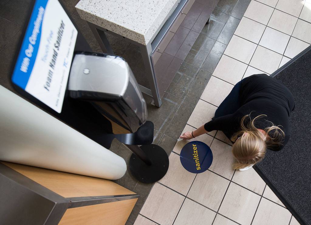 Property Management Assistant Larissa Chartrand smooths prepares a sanitizer sign while getting Alderwood mall in Lynnwood ready to open. (Andy Bronson / The Herald)