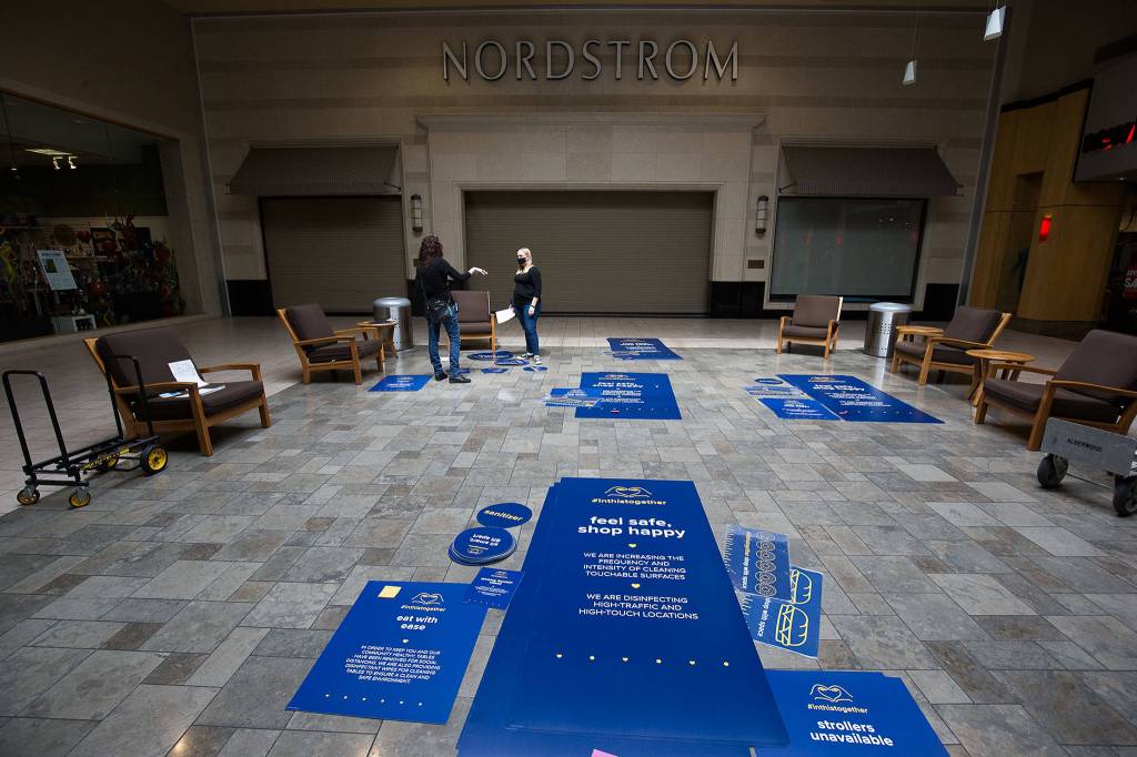 Property Management Assistant Larissa Chartrand (right) and Assistant Operations Manager Deborah Kearney organize signage as they get Alderwood mall in Lynnwood ready to reopen, hopefully in June. (Andy Bronson / The Herald)