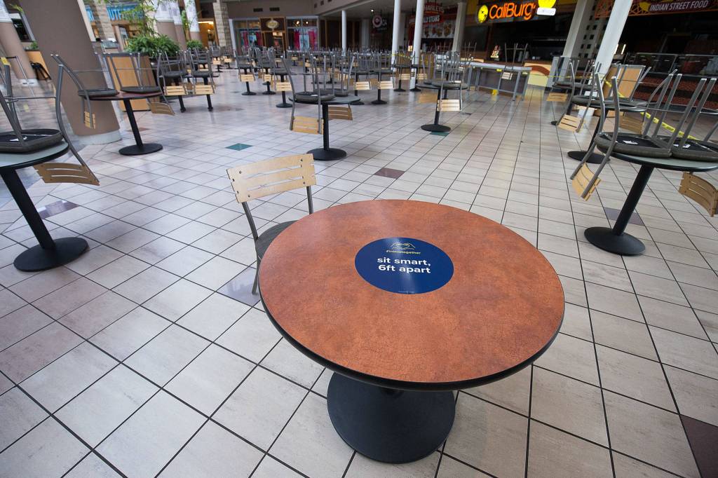 With many tables and chairs already removed for social distancing, a sign in the food pavilion at Alderwood mall in Lynnwood reminds diners to stay apart. (Andy Bronson / The Herald)